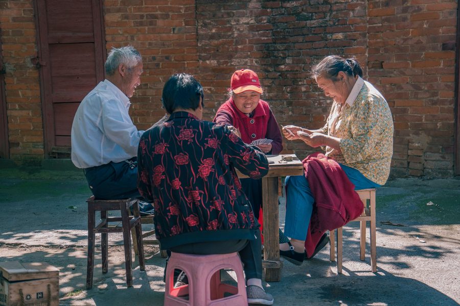 Four older players round a table in the sun, cards in hand